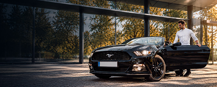 Schwarzer Ford Mustang Cabrio vor einer Glasfassade, daneben ein Mitarbeiter im weißen Hemd
